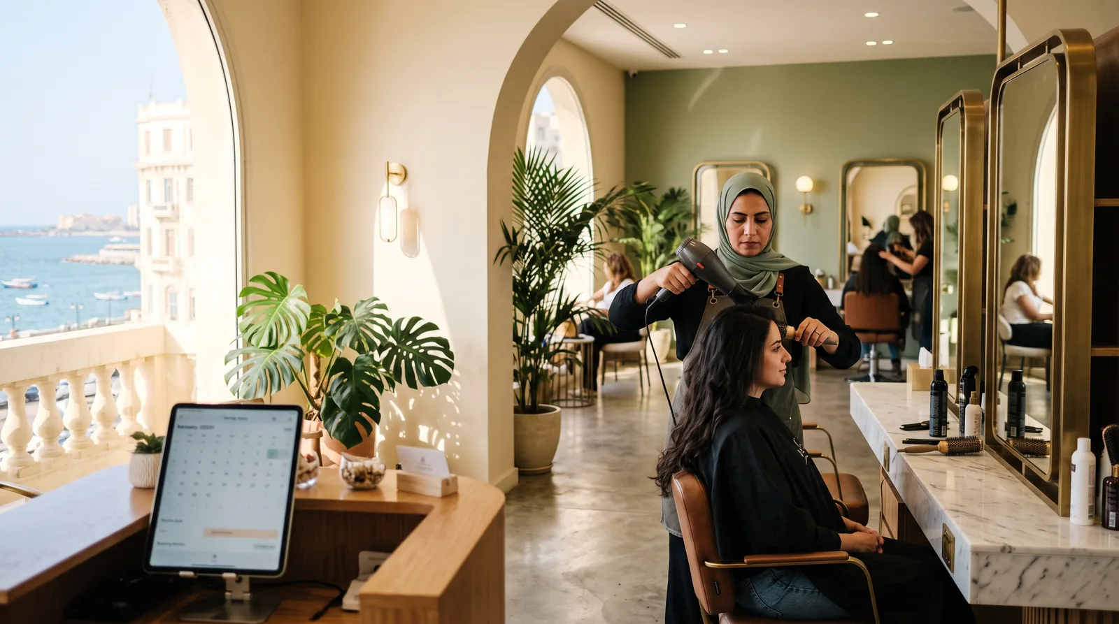 مصففة تجفف شعر عميلة في صالون تجميل مضيء في الإسكندرية ويظهر البحر المتوسط من النوافذ المقوسة